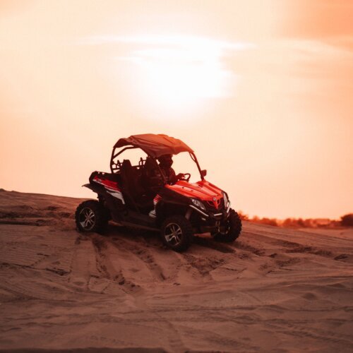 Red dune buggy driving in the desert at sunset